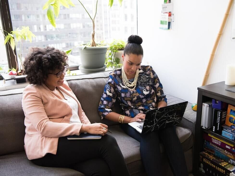 two black women working with laptop on a sofa